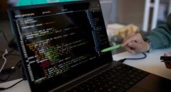 Focus on laptop screen with coded data and pen held by hand